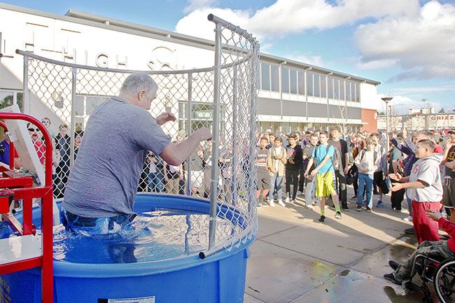 Rockne Roll/News-Register##McMinnville High School teacher Joe Crafton, left, slides into the dunk tank after a successful toss from freshman Nalen Stephens in front of the school Thursday, Jan. 28. The school placed a dunk tank in front of the building during lunch and after classes this week to celebrate the end of final exams.