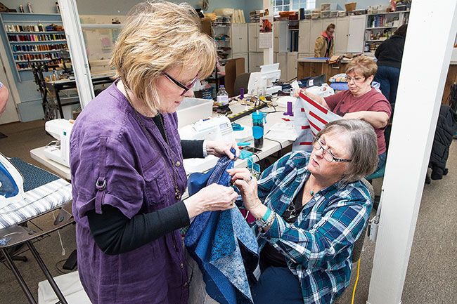 Marcus Larson/News-Register##Jane Petersen and Marlene Thomas discuss how to change the length of a piece of fabric as they finish a quilt top. They and other volunteers gather on Fridays to make Quilts for Cops.