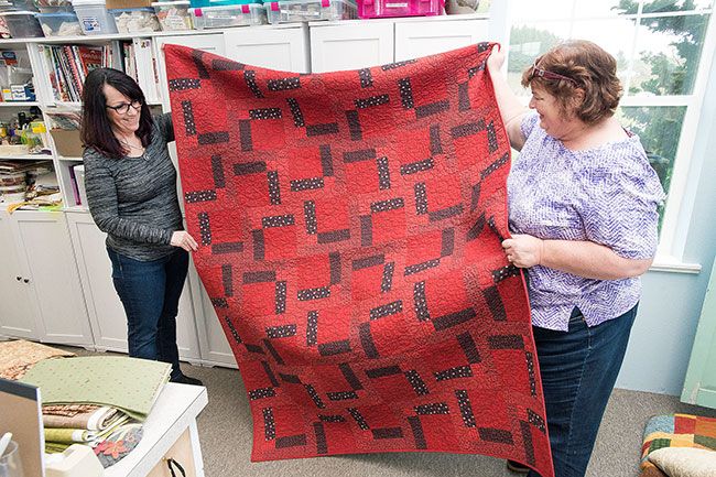 Marcus Larson/News-Register##Hope Sprunger and Bobbie Abernathy-Bebereia hold up a finished quilt that will go to a recently injured firefighter. The nonprofit provides comfort quilts for any first responder.