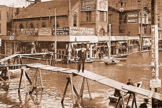 Image: Portland City Archives##Nattily dressed Portland businessmen carry on during the 1894 flood, using a makeshift bridge to cross flooded Third Street at the intersection with Washington Street. Image: Portland City Archives##Nattily dressed Portland businessmen carry on during the 1894 flood, using a makeshift bridge to cross flooded Third Street at the intersection with Washington Street.