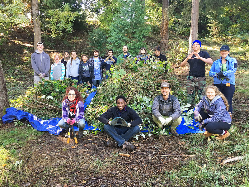 Submitted photo##Local community members and students from Linfield College and Chemeketa Community College pose with a pile of invasive weeds removed from along Cozine Creek on Linfield Campus. Linfield is working with the Greater Yamhill Watershed Council to secure grant funding to enhance the habitat on Cozine Creek on campus, and to engage the community in service learning activities.