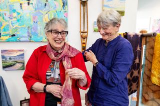Rusty Rae/News-Register##Ilsa Perse, right, drapes one of her scarves around the neck of Phyllice Bradner, one of her partners in the Currents Gallery on Third Street. Bradner, Perse and five other artists own the gallery, which will mark its 20th anniversary this weekend. Rusty Rae/News-Register##Ilsa Perse, right, drapes one of her scarves around the neck of Phyllice Bradner, one of her partners in the Currents Gallery on Third Street. Bradner, Perse and five other artists own the gallery, which will mark its 20th anniversary this weekend.