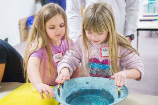 Rusty Rae / News-Register##

Adelyn Jaeger, right, rubs her dampened palm along the edge of a basin
of water, held by Alice Walters. The movement causes little waves, as
well as a humming sound.