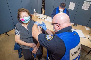 Marcus Larson/News-Register##Guadalupe Najar receives a Moderna COVID-19 vaccine from Tualatin Valley Fire & Rescue paramedic Jason Schurter with computer assistance from William Harmon during a recent vaccine clinic at the Yamhill County Fairgrounds.