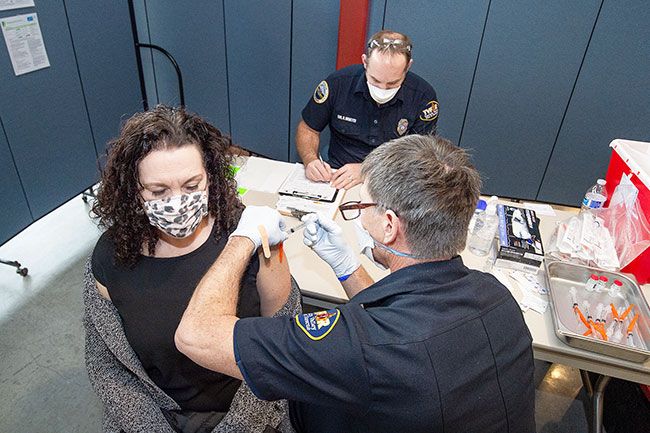 Marcus Larson/News-Register##Sue Buel Elementary third grade teacher Laura Hyman gets her first COVID-19 vaccine shot from TVF&R paramedic Brian Pine with assistance from Ryan Niemeyer, during McMinnville School District s vaccine clinic.