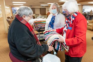 Marcus Larson/News-Register##American Legion Auxiliary members Carol Doege, right, and Susan Haley, center, hand veteran Annie Gholz a crocheted Valentine’s Day lap robe to thank her for her years of service in the Navy. Gholz was one of about 20 vets the McMinnville Auxiliary members met at Brookdale Senior Living; they also take gifts to vets in other care centers.