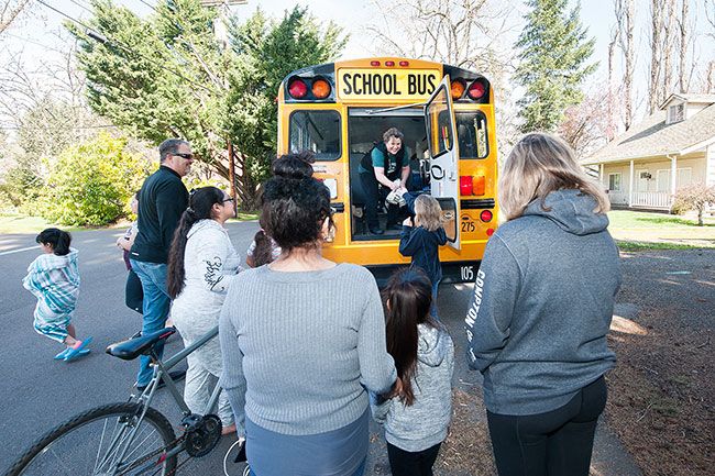 Rusty Rae / News-Register##Parents and children gather at the back of a school bus to receive grab-and-go meals from Karen Nichols and other school employees. Food can be picked up at elementary schools or at bus stops.