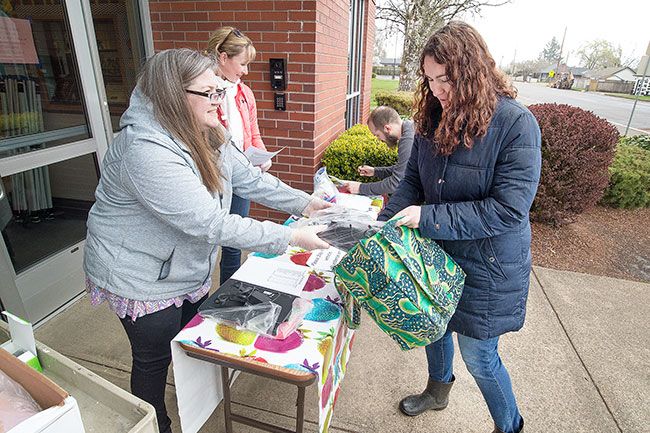 Marcus Larson/News-Register##At the Memorial Elementary School pickup site, volunteer Michelle Morain hands parent Breeayn Ardianto a Chromebook for checkout.  Students can keep the devices as long as schools remain closed.