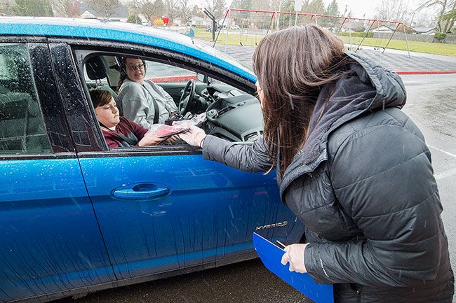 Marcus Larson/News-Register##At the Memorial Elementary School pickup site, volunteer Michelle Morain hands parent Breeayn Ardianto a Chromebook for checkout.  Students can keep the devices as long as schools remain closed.