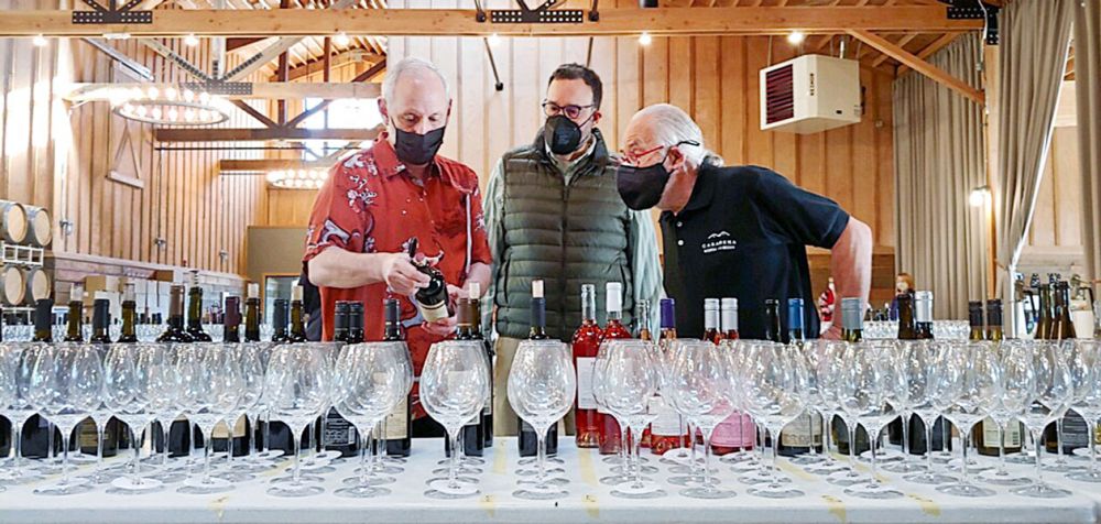 Submitted photo ## 
Mike Miller, coordinator of the Sip! McMinnville Food & Wine Classic wine competition, left, considers a bottle of wine with Carl Giavanti, competition publicist, and Rolland Toevs, competition manager during the event Saturday, March 27, at Abbey Road Farms. About 200 Oregon wines were entered in the 2021 event.