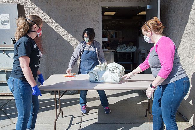 Marcus Larson/News-Register ##  Johnson, center, brings out trays of lunches for volunteers Mandy Den, left, and Dana Symons, right to load on to school buses. Families can pick up food at bus stops or from the high school cafeteria.