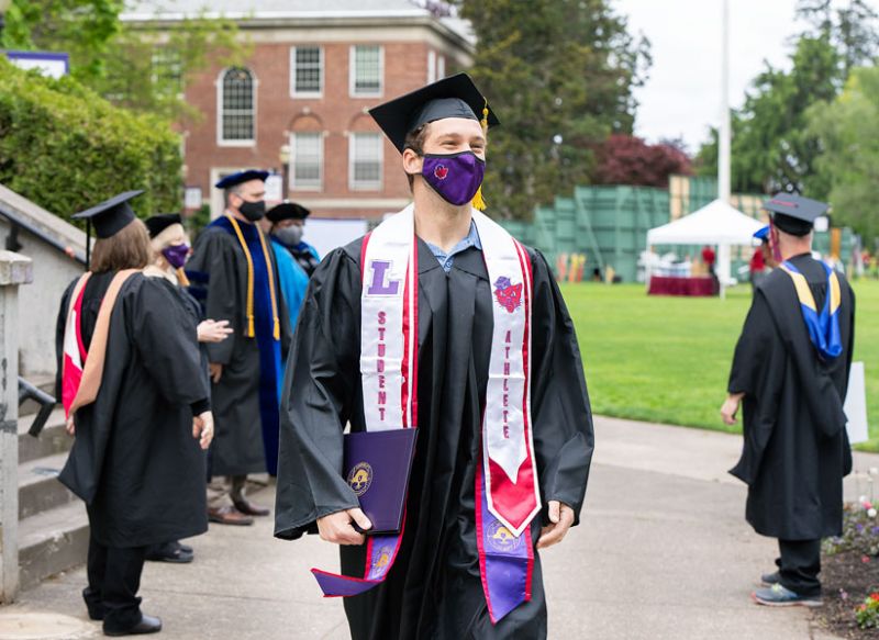 Marcus Larson/News-Register ##
Newly graduated Cooper Bousquet smiles behind his mask as he talks with Linfield University professors lined up in a gauntlet to congratulate him Sunday morning. Bousquet’s parents and grandfather also graduated from Linfield.