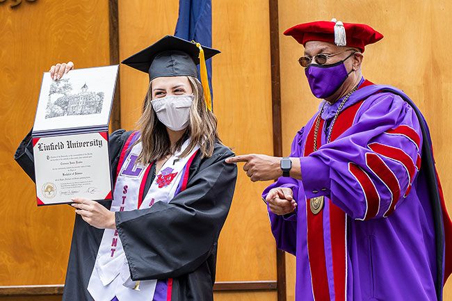 Marcus Larson/News-Register ##
Cameron Reuter proudly shows her marketing degree to her parents, who follow her through the commencement path in in their cars.