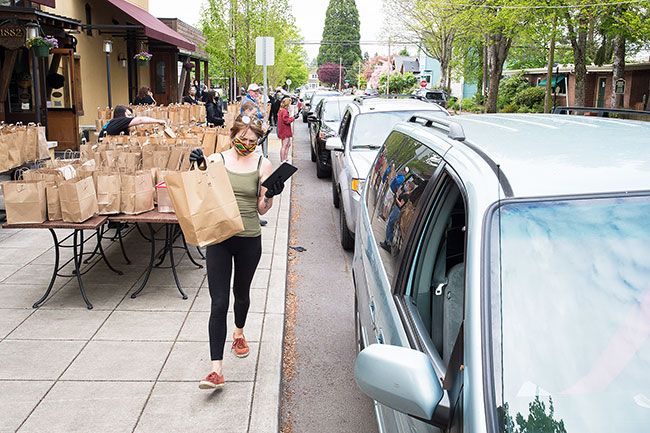 Marcus Larson/News-Register##Nikia Walker carries a food order to a waiting car in line during the 1882 Grille community dinner event, celebrating the restaurant s reopening.