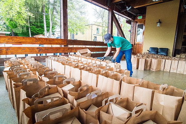 Marcus Larson/News-Register##Joshua Jennings sorts through hundreds of bags of food to and replenish the ones in front of the KAOS building in downtown McMinnville, waiting to be picked up by locals taking advantage of the 1882 Grille s free meal giveaway last Friday.