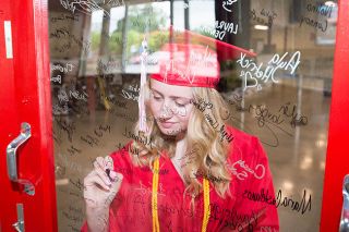 Marcus Larson/News-Register##McMinnville High graduate Peyton Burke takes a moment to write her name on the photo booth wall after having her graduation photo taken Monday morning.