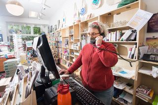 Rusty Rae/News-Register##Third Street Books owner Sylla McClellan processes an order over the phone. Although her retail shop is allowed to open today, McClellan said she will take a couple weeks to adjust the layout of the store before permitting walk-in traffic.