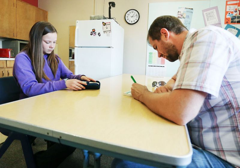 Rockne Roll/News-Register##Kaylee prepares to test her blood sugar as her teacher, Michael Buehler, makes an entry in her file Wednesday, May 31, at Yamhill-Carlton Intermediate School in Yamhill. Y-C sixth graders received an ice cream treat as a reward for their collective good behavior at Outdoor School; Williams, who was unable to attend, had to administer insulin before joining her classmates in their reward.