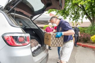 Rusty Rae / News-Register##Jim Botten loads a box of food into a client’s car Friday as a part of the St. James food box giveway. In the background in the red is John Deagas. Also in the background is Father Mike Walker. This event will continue each Friday throughout June. Rusty Rae / News-Register##Jim Botten loads a box of food into a client’s car Friday as a part of the St. James food box giveway. In the background in the red is John Deagas. Also in the background is Father Mike Walker. This event will continue each Friday throughout June.