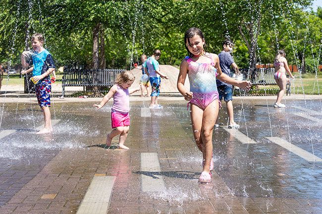 Marcus Larson/News-Register
##Eight-year-old Avry Thresher is chased by her friend 3-year-old Zarayah Root while playing in the Discovery Meadows Park “splash pad” on a hot Wednesday afternoon. The fountain will be open over the weekend, when temperatures are forecast to soar over 100 degrees. Several cooling centers also will be open to help people beat the heat.