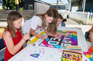 Rusty Rae/News-Register##Hanna and River Frankamp and Cooper Oaks add bright colors to a poster proclaiming “You Are Loved” during the first Pride Street Fair. Saturday’s fair was one of numerous activities held during Pride Month.