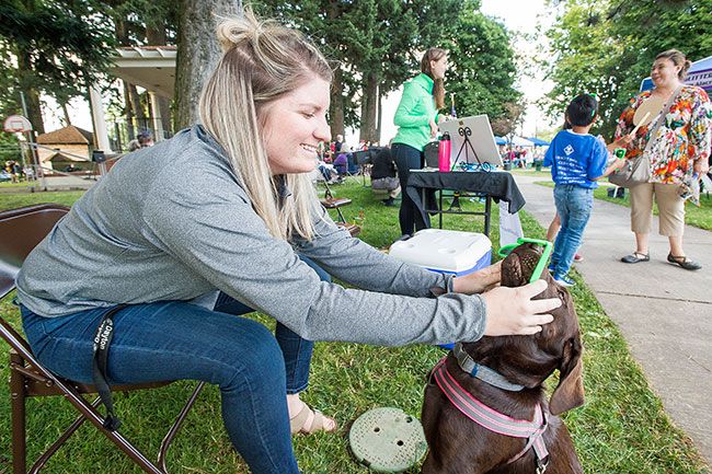 Marcus Larson/News-Register##
Hanna Palo with First Federal tries to get her dog Pepper to wear a pair of green sunglasses during the Dayton Friday Nights event.