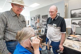 Marcus Larson / News-Register##Chuck Rogers, right, and Dave Pfendler share a laugh as Ingrid Palm looks through a stereoscope at a photo of the Dayton Blockhouse with a dinosaur digitally added to the scene.