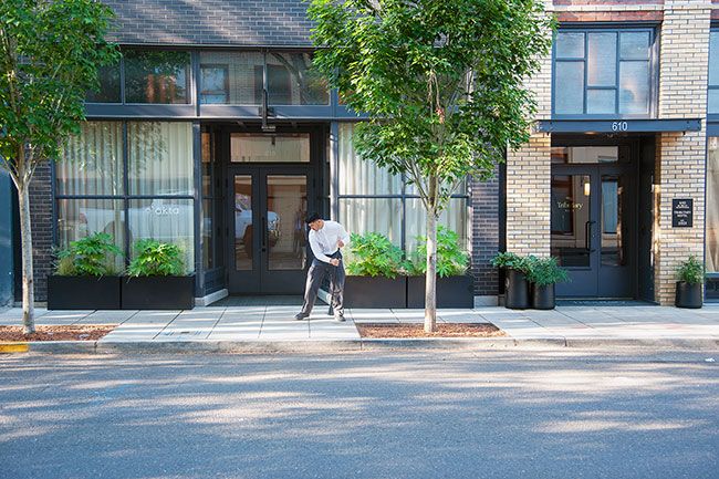 Kirby Neumann-Rea##Tributary Hotel valet Chris Marquez sweeps the sidewalk early Thursday in preparation for guests at the hotel, entry at right, and okta restaurant,left. Tree wells in front of the hotel and restaurant are filled with hazelnut shells.