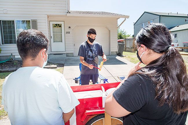 Marcus Larson/News-Register##  Miguel Lozano prepares elotes, a traditional Mexican street food, for customers Johan Veles and Karen Velez.