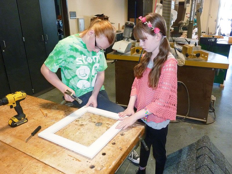 Starla Pointer / News-Register##Lorelai Kitt holds a piece of plexiglass in place as Emily Phipps secures into a door frame for one of the little libraries.