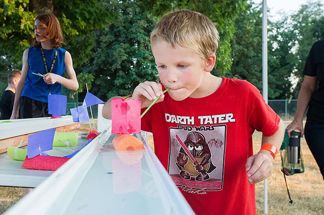 Marcus Larson/News-Register##Liam Christensen blows on the sail of his foam boat to propel it down a water-filled gutter during Lafayette s 2018 National Night Out event.