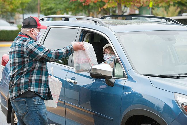 Rusty Rae/News-Register##McMinnville High School junior Nicole Aquinas receives a swagbag of school supplies from English language teacher Christopher Staff during a drive-by distribution on Wednesday.