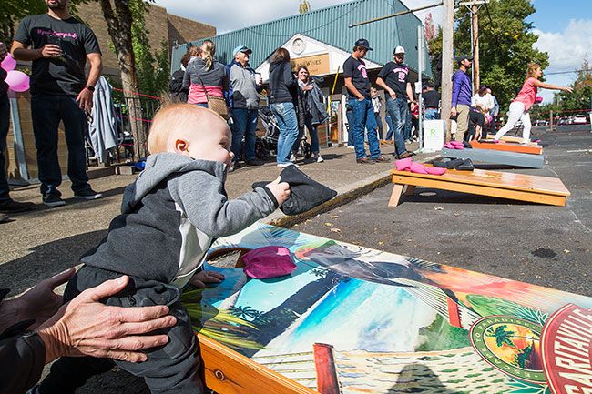 Marcus Larson / News-Register##During the tournament, 14-month-old Tyson Smalley tries to participate by grabbing the pink and black bean bags and throwing them.