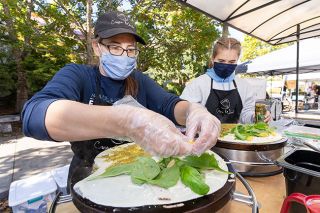 Marcus Larson/News-Register##Crepe World owner Jamie Akers and assistant Anna Dazey each make a Ravenna-style crepe with chicken, pesto, tomatoes, spinach and cheese at the McMinnville Farmers Market.