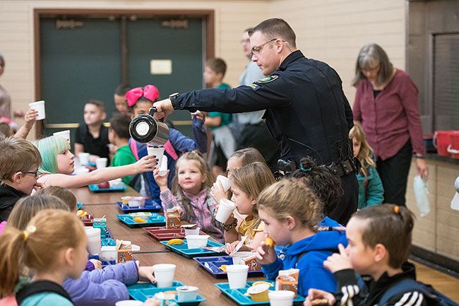 Rusty Rae/News-Register ##
Carlton police officer Jake Blair pours warm chocolate milk for children during breakfast at Yamhill-Carlton Elementary School last week. Later, Blair played “The Star Spangled Banner” on his electric guitar, a la Jimi Hendrix.