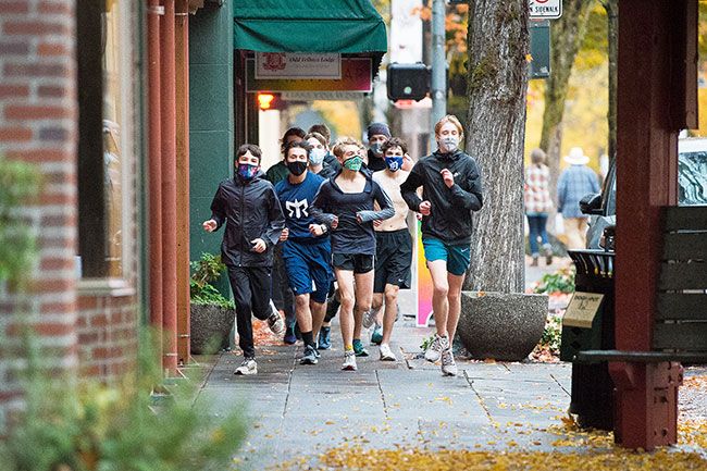 Marcus Larson/News-Register##Members of the McMinnville High School cross country team jog on Third Street wearing masks last month. School board members praised the students and their coaches for taking safety precautions as they return to practices. Other fall sports teams and those from winter and spring also are practicing skills and teamwork one or two afternoons a week.