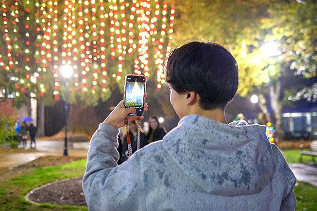 Rusty Rae/News-Register##Linfield exchange student Yudai Hamaski takes a photo of the lit Christmas tree in downtown McMinnville with three of his friends Friday. The foursome braved the rain showers to experience the annual holiday parade and tree lighting festival.