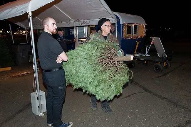 Rusty Rae/News-Register##Eric Trammell of McMinnville watches as Todd Caster, a member of the McMinnville Lions Club, carries a tree to Trammell’s vehicle. Trammell and his wife, Susanna Rose, were among the last customers Wednesday at the Lion’s tree lot near Sears.