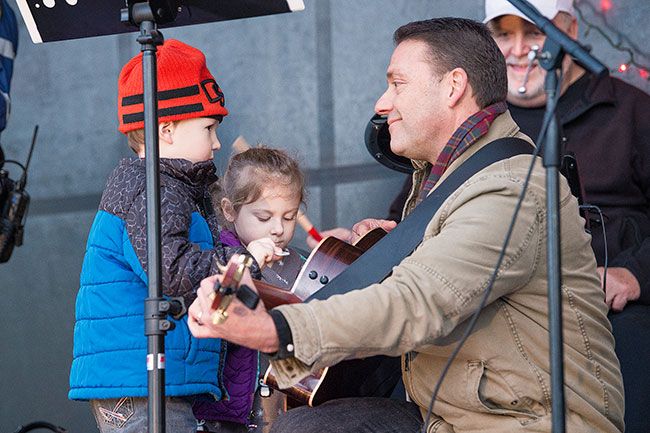 Marcus Larson / News-Register##While performing on stage in Ladd Park, Carlton police chief Kevin Martinez gets some guitar-playing help from Hope Dalton and Oscar Lefebvre.