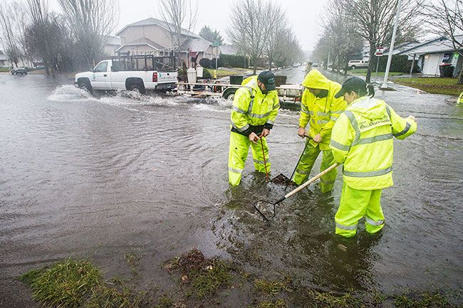 Marcus Larson / News-Register##McMinnville Public Works employees Jeff York, Michael Payne and Liz Fliszar try to clear storm drains at Fellows and Oriole streets as flood waters rise Monday.