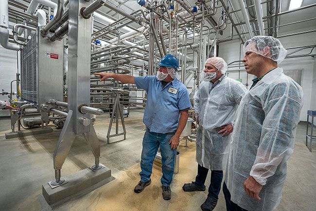 Rachel Thompson/News-Register##Local Maintenance Manager Paul Silva, left, Organic Valley CEO Jeff Frank and Mark Pfeiffer take a look at a room filled with small pipes, through which milk flows to become pasteurized. A large, square heater on the left was saved from the rubble and refurbished to be used in the newly built creamery.