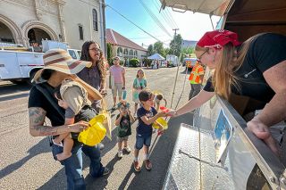 Rachel Thompson/News-Register##Nicole Lynn Tignor hands a Sno-cone to Kaz Lampman, attending the city’s Community Fair Thursday with parents Ana and Jason and siblings Rad and Arrow. Dig Safely Oregon was one of several organizations with booths and trucks set up at the event.