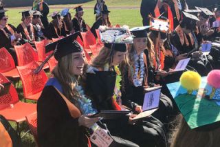Kirby Neumann-Rea/News-Register##Yamhill Carlton graduates read their diplomas for the first time on the sunny, windy high school football field. Calli Jordahl, left, laughs with class president Kya Ellis, far right. At center is Briley Ingram, and to her left is Alysse Hurley.