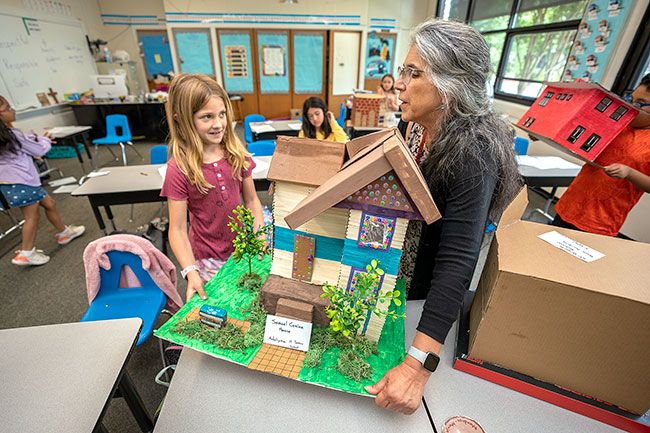 Rachel Thompson/News-Register##St. James School second/third-grade teacher Donna Carlisle helps Adelynn Moore lift the student’s model of the Cozine House. The 1892 building started life as the home of Samuel Cozine, and now holds the McMinnville Downtown Association office.