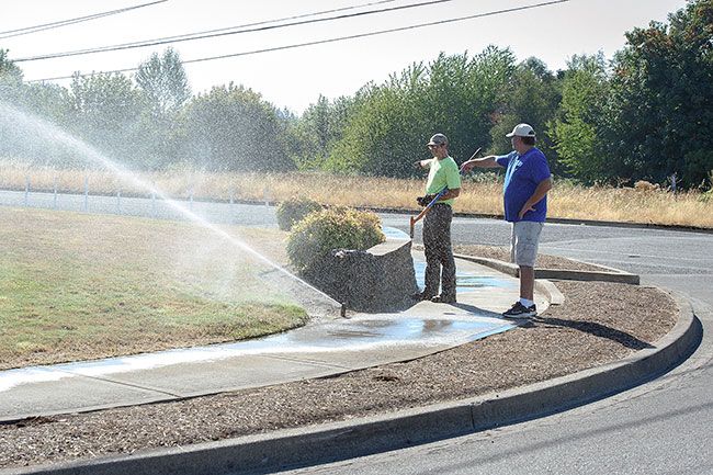 Rusty Rae/News-Register##Owner Andy Rhodes (right) of A R Landscape, works with foreman Jeff Burton during a Monday morning watering session for the recently planted lawn at the corner of Northeast Alpha Drive and Riverside Drive.