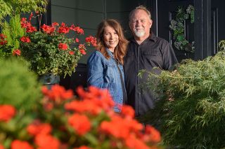 Rusty Rae/News-Register##Jan Schmidt and Brad Buchanan look out from the porch of their home on Northwest 19th St., which won Yard of the Month honors for September. Schmidt chose her favorite color, orange, to surround the lawn, adding purple flowers accents.