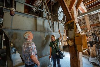 Rachel Thompson/News-Register##Craig Pubols watches as Mindy Legard Larson demonstrates overhead grain mixing machinery on the second floor of Buchanan Cellers. Clipboards, notes, labels and machinery manuals unused in years remain in place throughout the mill.