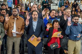 Rusty Rae/News-Register##Sixty new citizens who hail from 19 different countries stand to pledge their allegiance to the United States. They went through a naturalization ceremony Nov. 9 at the Evergreen Space Museum.
