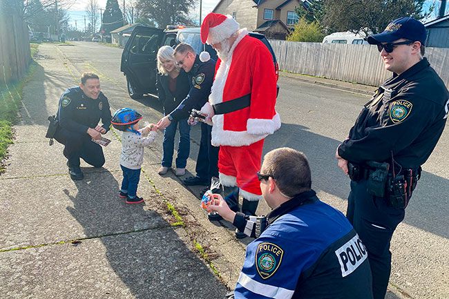 Starla Pointer/News-Register##Officer Jake Blair, center, hands a bag of treats Saturday to David Lee Russell, 1, during the Carlton police department’s annual Santa Patrol event. David was on a walk with his mother, Christie Russell, when officers and Santa stopped to visit with him. Also pictured, from left, are Chief Kevin Martinez, Christy Martinez, and officers Tim Jordan and Micah Steeves.