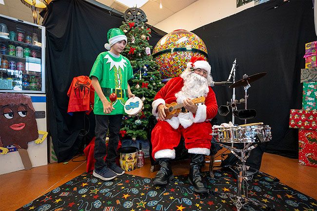 Rachel Thompson/News-Register##Santa Sal Solano and Elf Tristen Brink, 11, sing “Feliz Navidad” as they greet customers in the “Hispanic Musical Santa” event Saturday at The Reel Hollywood Video store in McMinnville. The shop’s giant gumball machine complemented the Christmas decorations in the store. Children visiting with Santa got to sing along or play the maracas or tambourine, and the elves gave out candy canes. Kids could get their photo taken with Santa for a donation that went to The Soup Kitchen @ St. Barnabas.